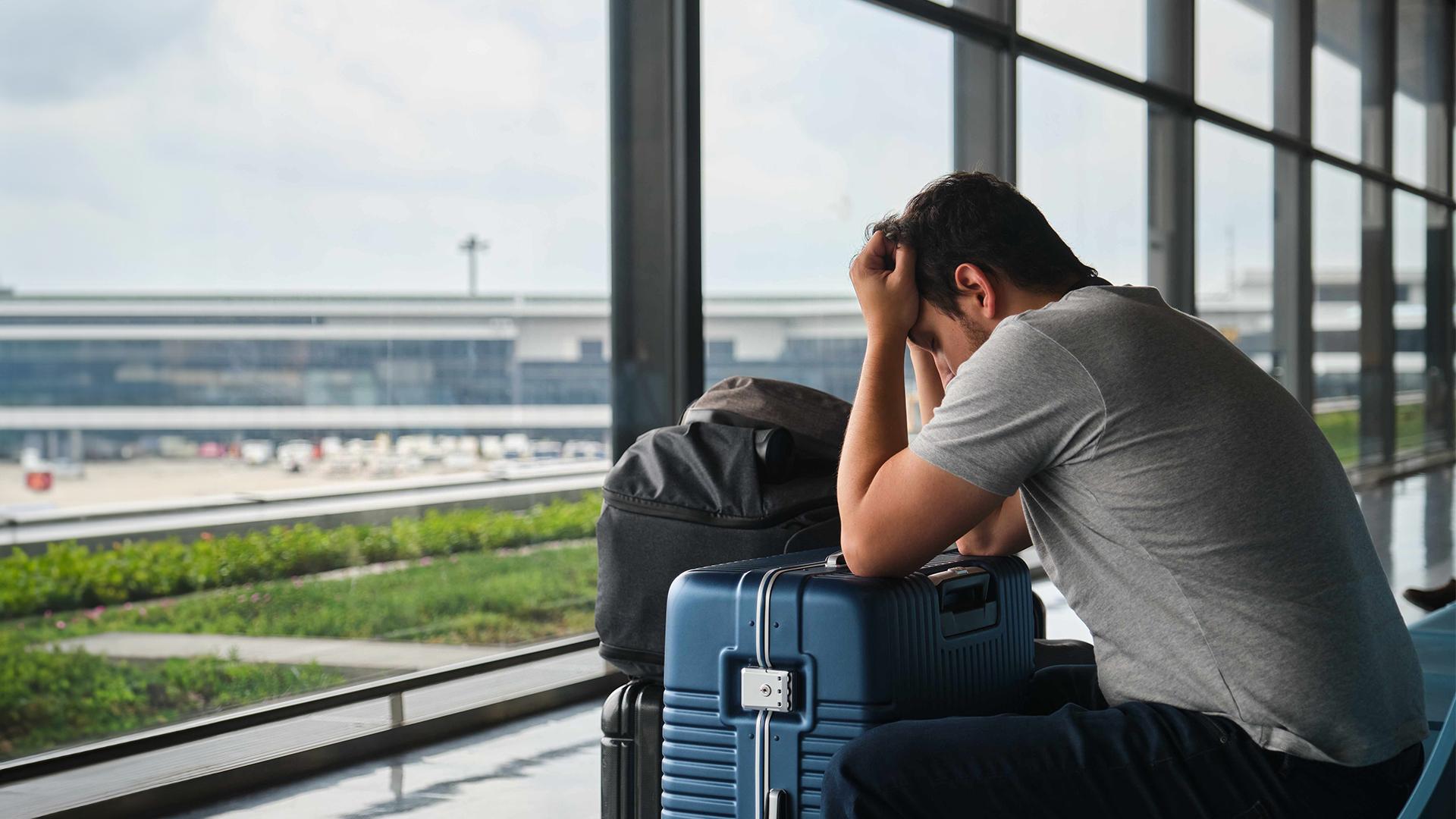 Un voyageur patiente à l’aéroport et se tient la tête dans les mains, l’air tracassé.